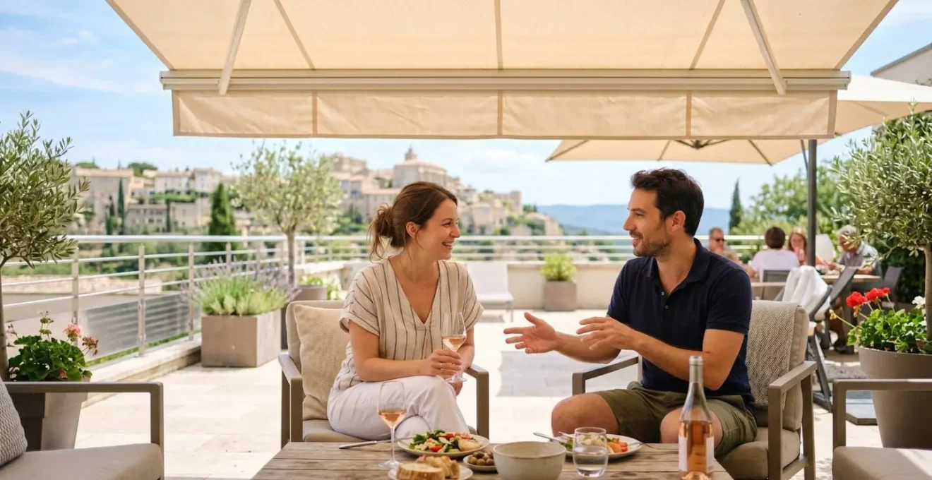 Un couple vu de dos profite d'une terrasse moderne sous un store banne déployé, l'un assis avec une tablette, l'autre debout regardant le jardin, lumière tamisée par la toile créant une atmosphère apaisée malgré le soleil éclatant à l'extérieur